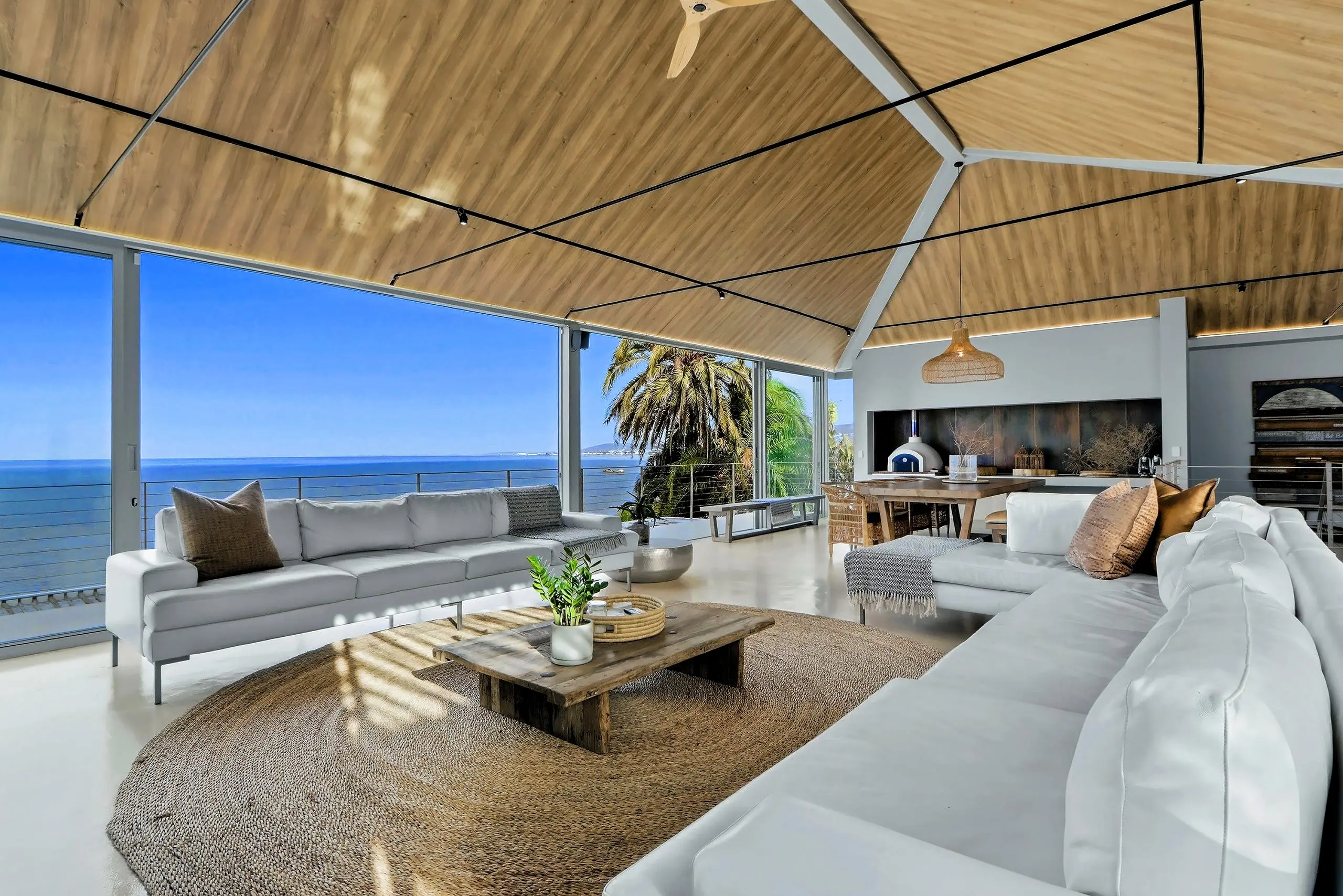 Lounge with white sofas and a jute rug facing floor-to-ceiling glass and the open sea