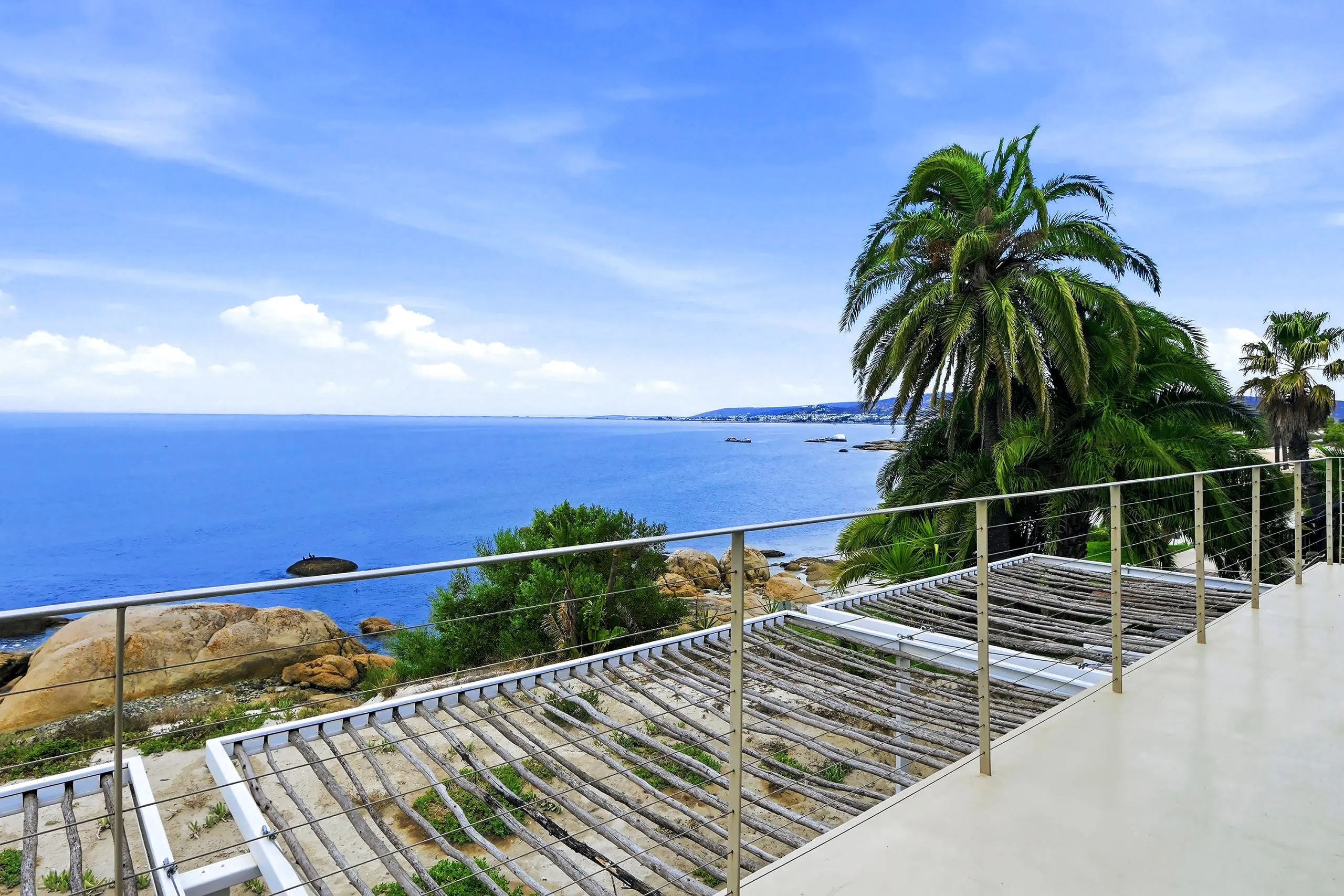 Terrace balustrade above granite boulders and the calm bay, with palms and the far shore