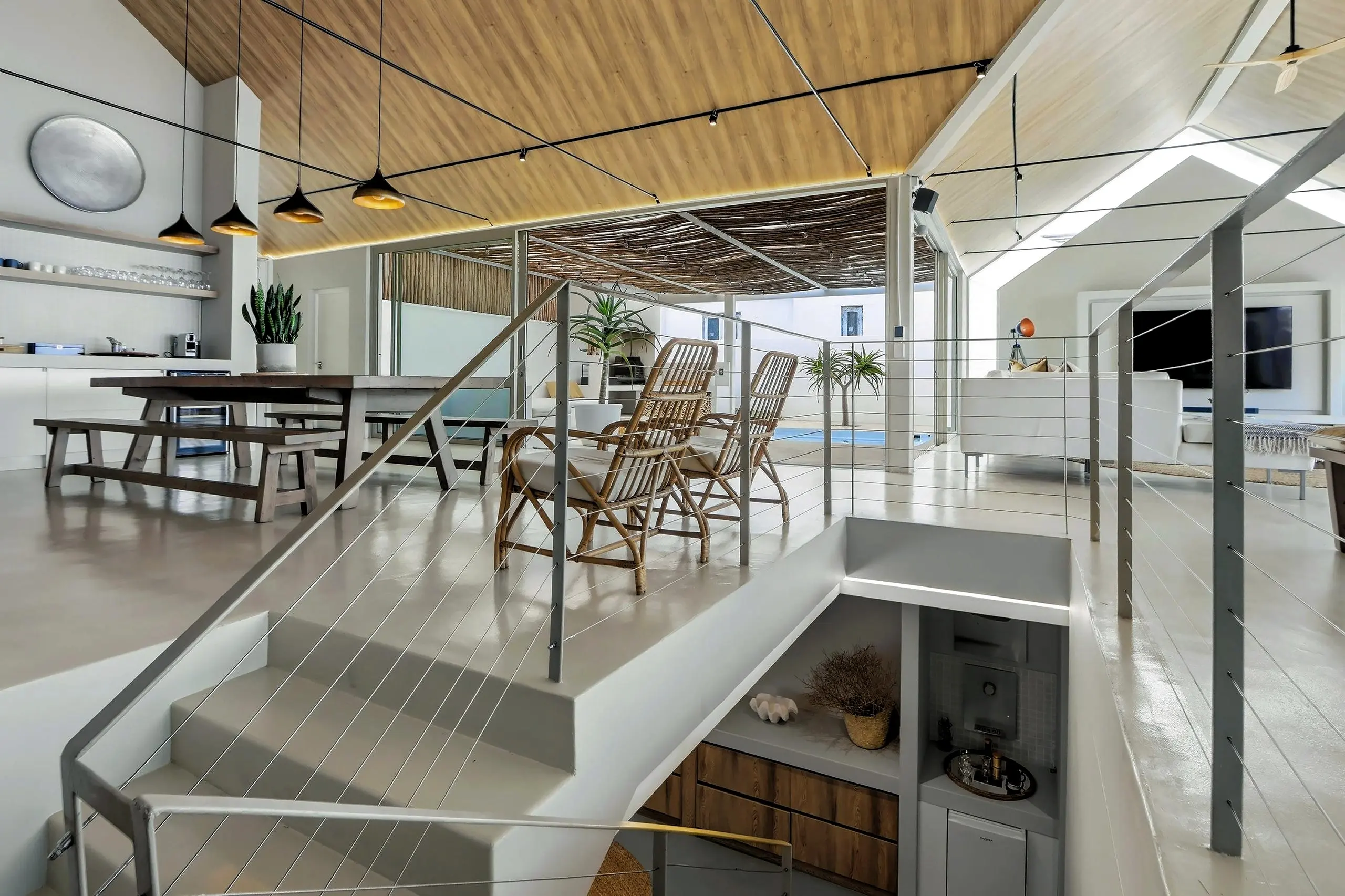 Steel-and-cable staircase beside the dining area, rattan chairs and the pool courtyard behind