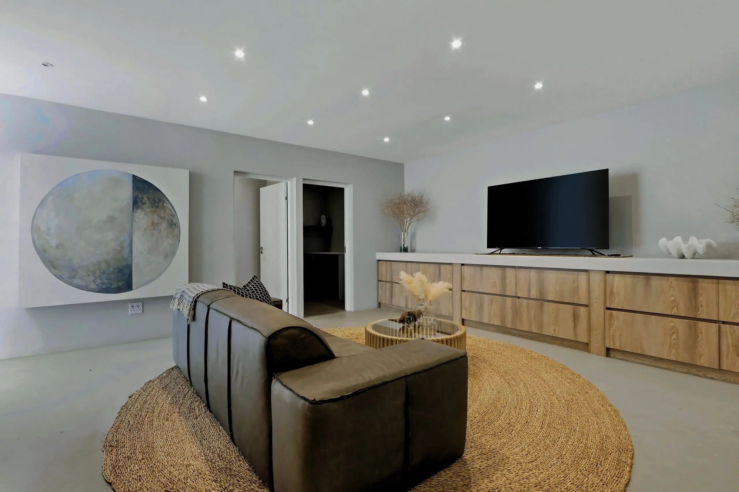 Downstairs lounge with a leather sofa, oak cabinetry, a TV and a large round artwork