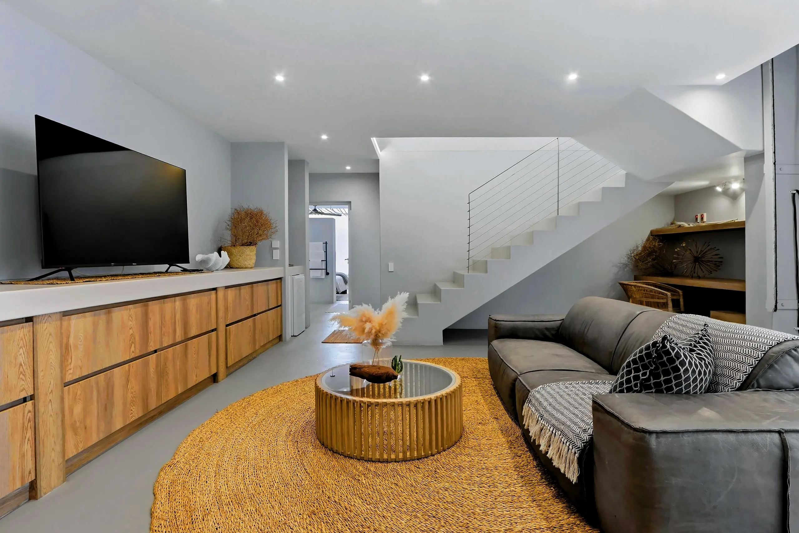 Downstairs lounge with grey sofa, oak media unit and the open staircase to the living floor