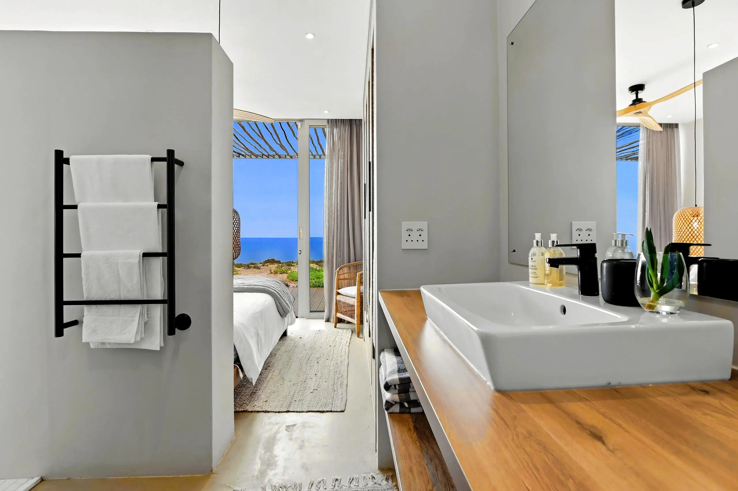 Bathroom vanity with a timber counter looking through to the bedroom, deck and ocean