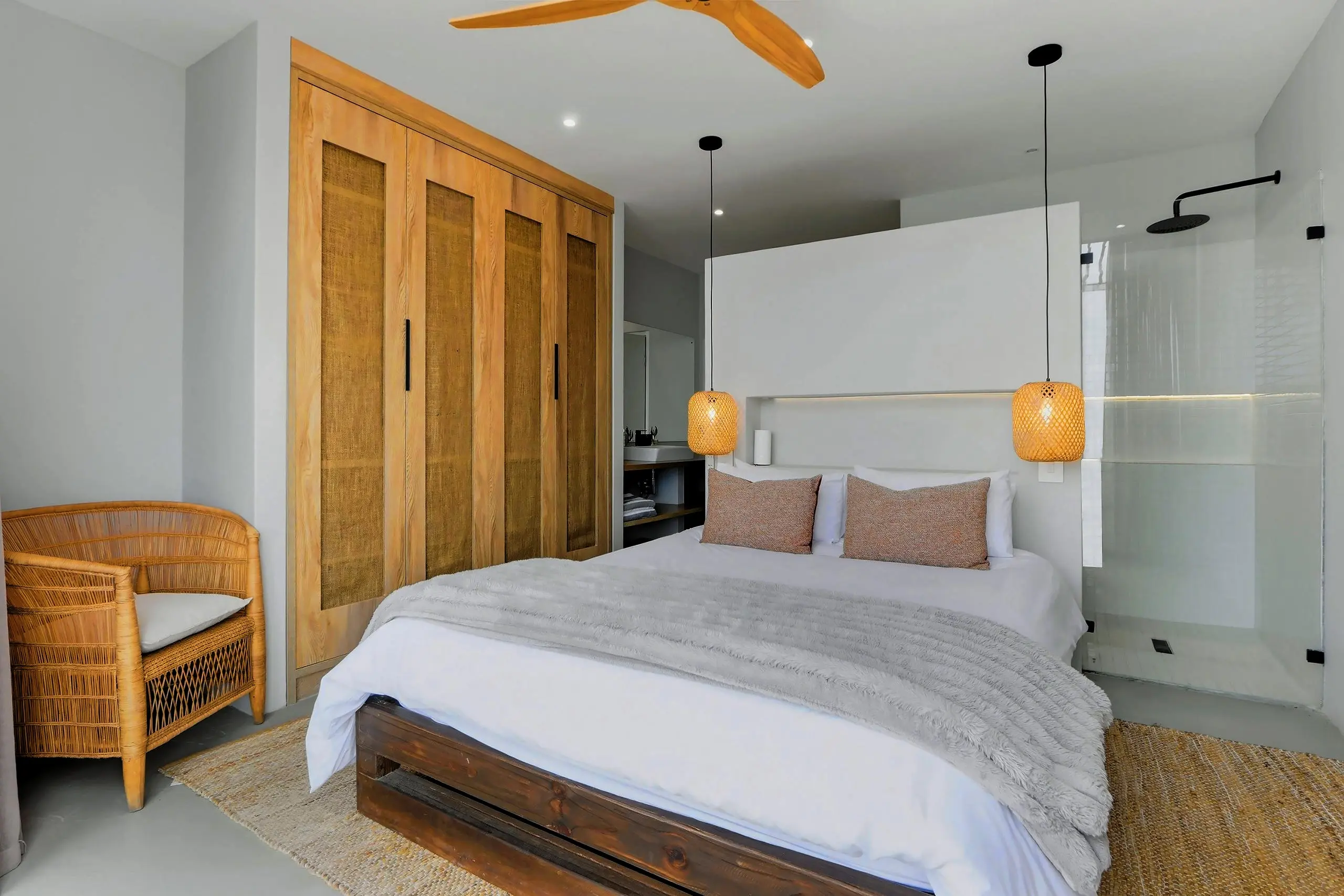 Bedroom with hessian-panelled timber wardrobes, rattan chair, pendants and an open glass shower