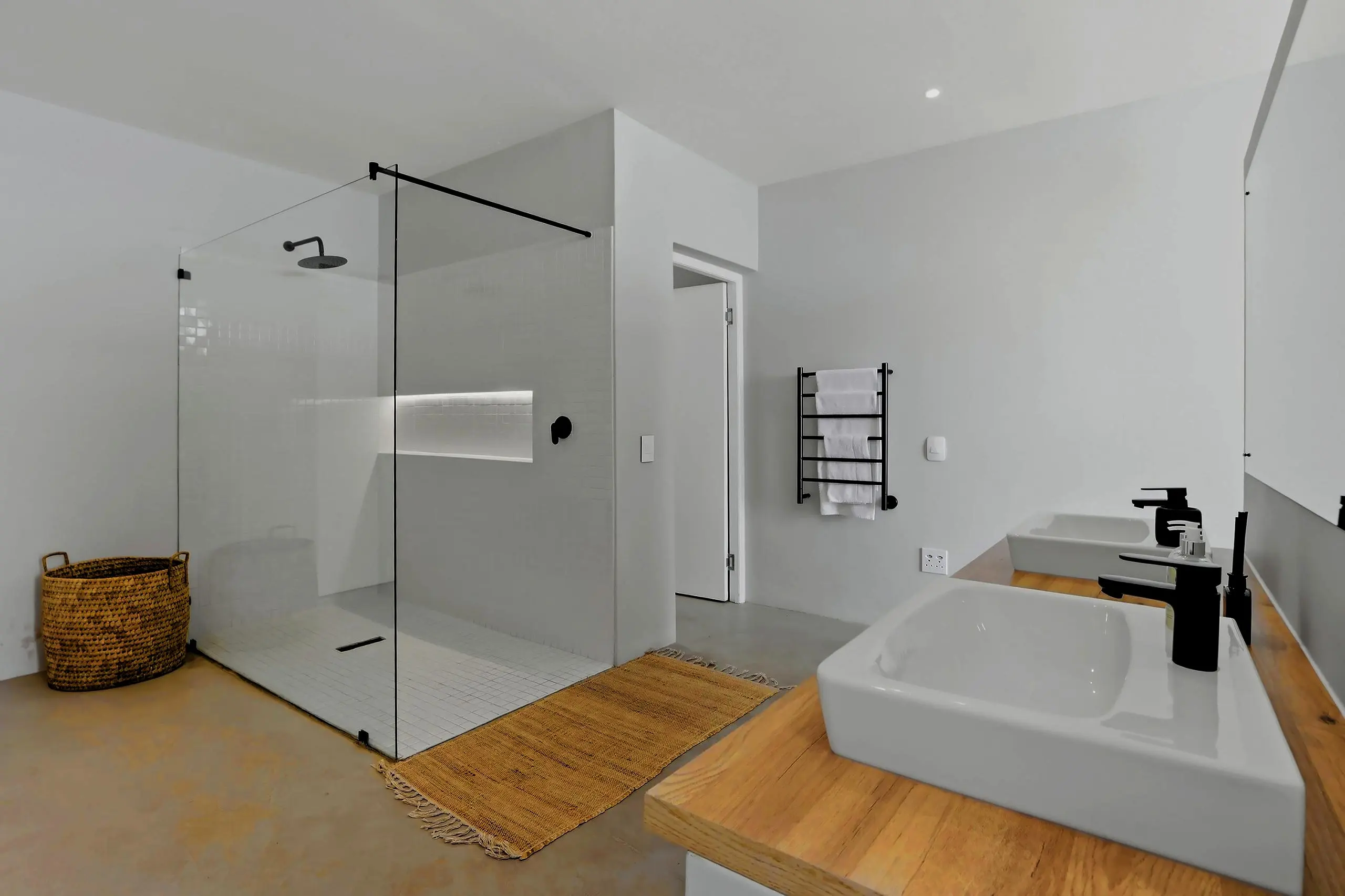 Glass-walled shower, double basins on a timber counter and a basket on the floor