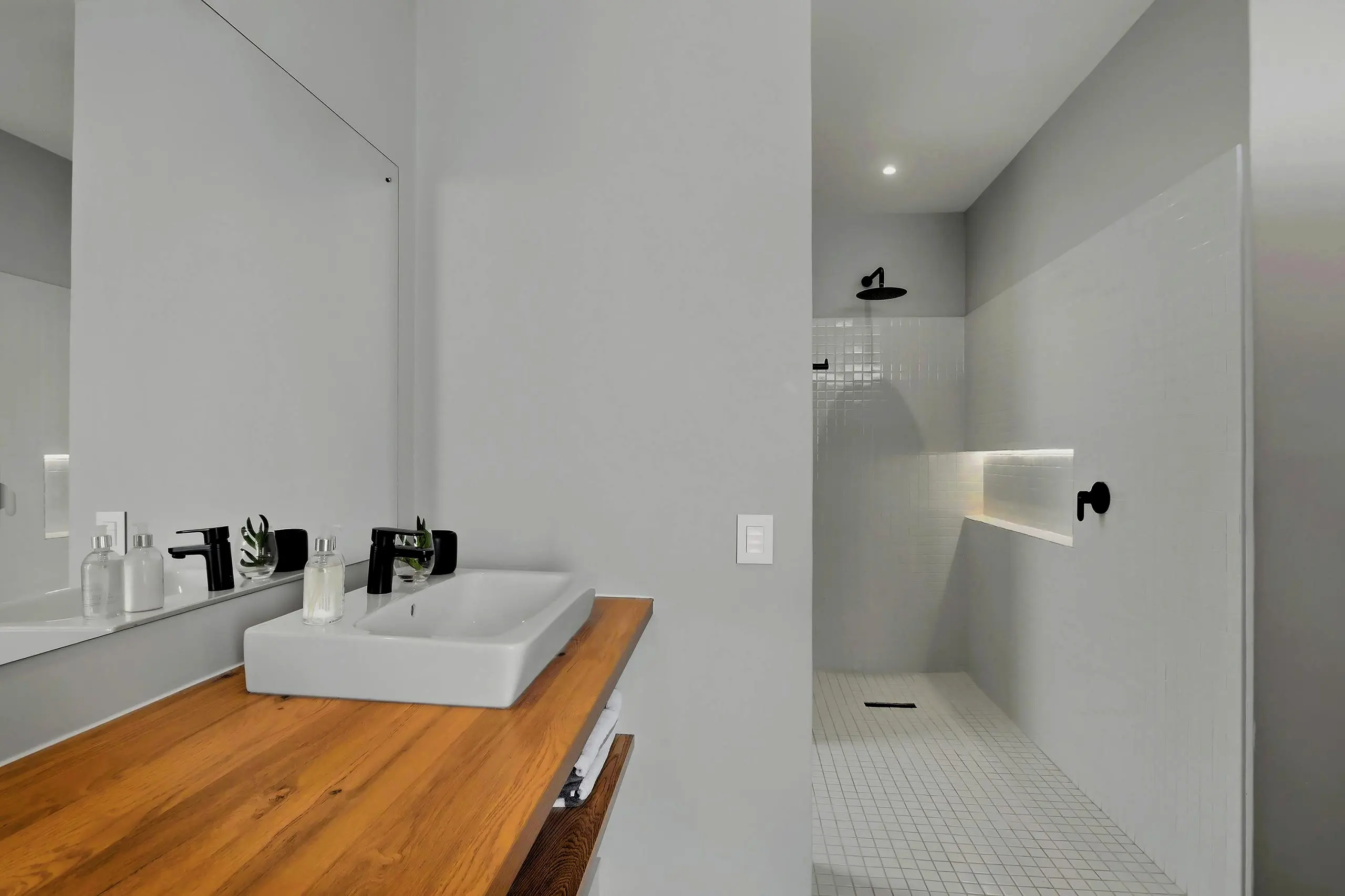 White-tiled walk-in shower with a rain head beside a timber vanity