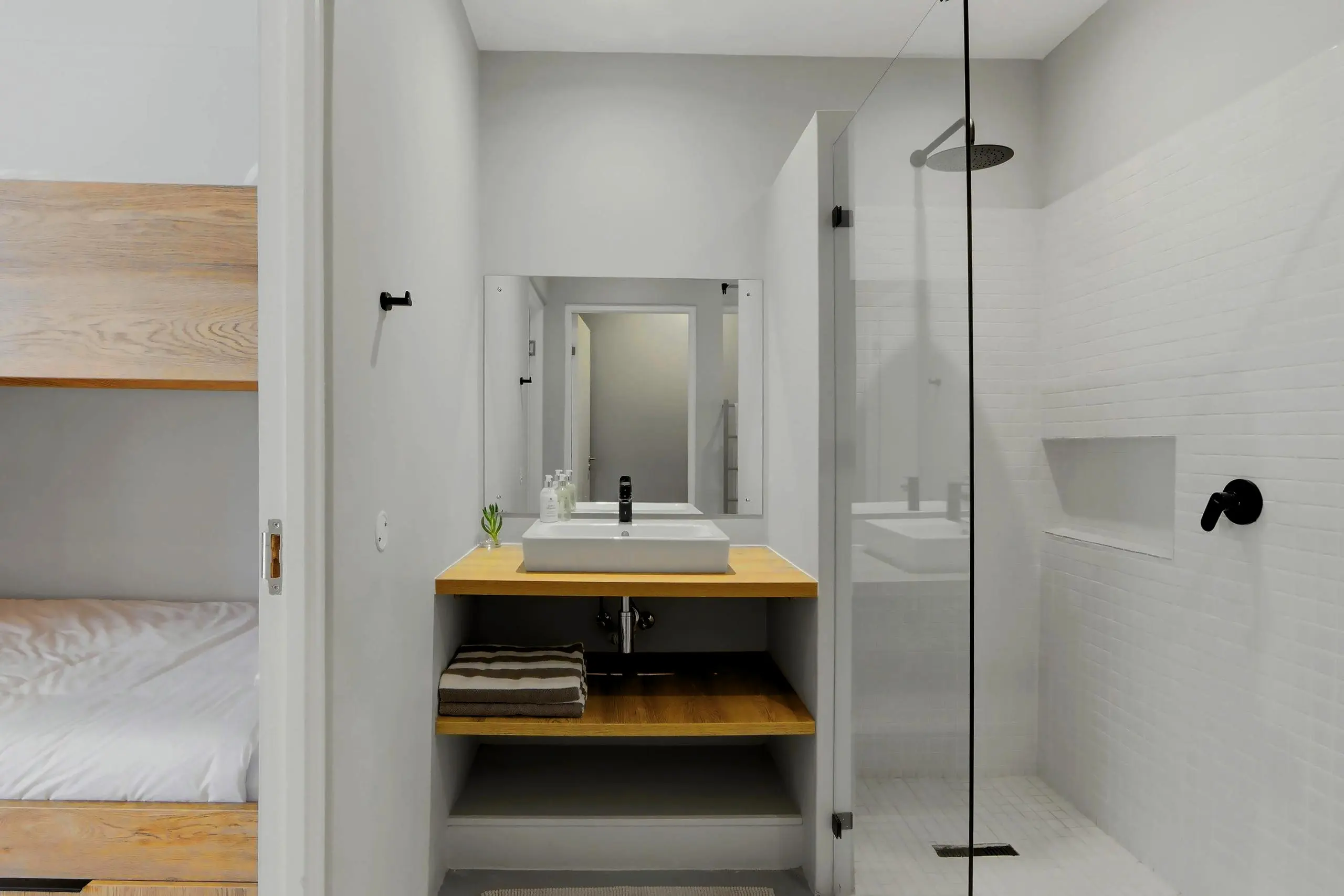 Compact en-suite with basin, timber shelf and glass shower next to the bunk room