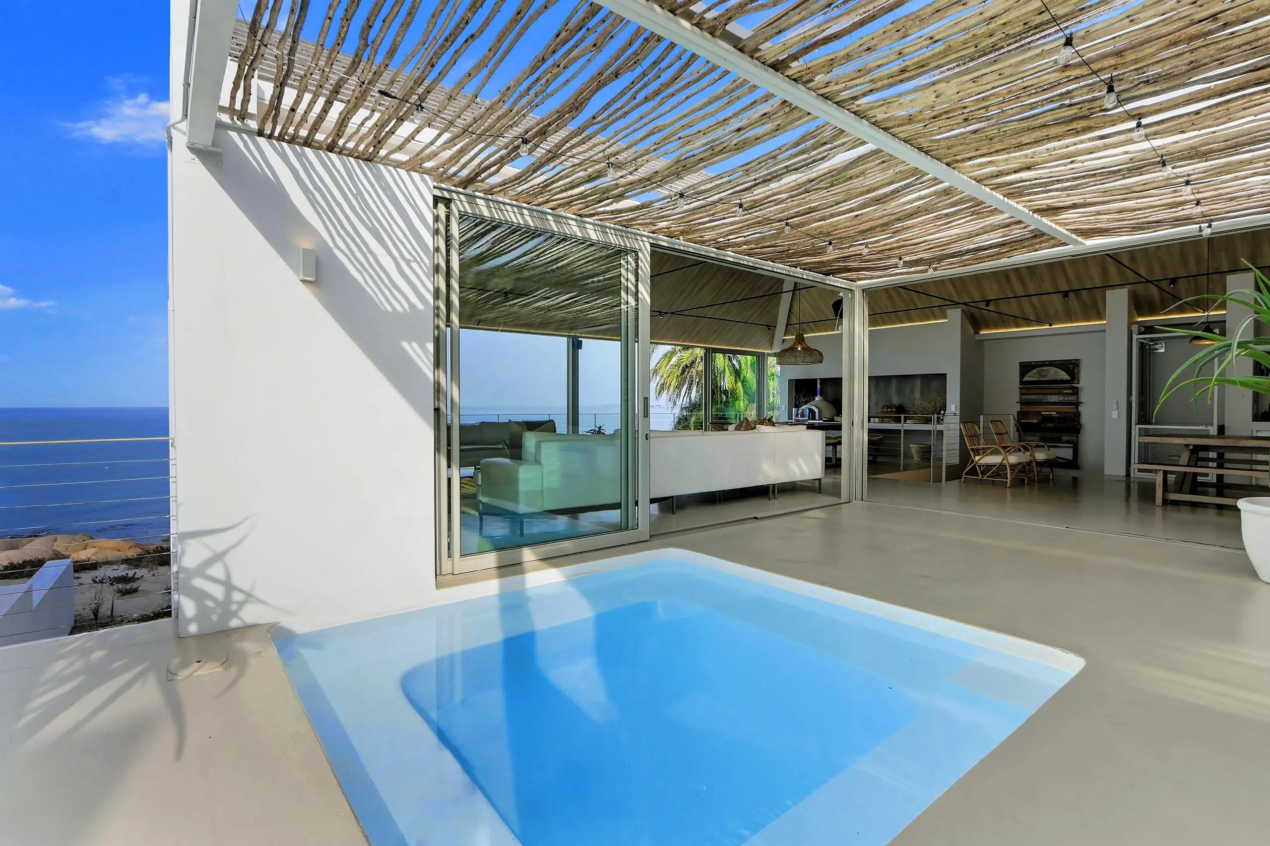 Plunge pool under a latte-wood pergola with the lounge and ocean beyond