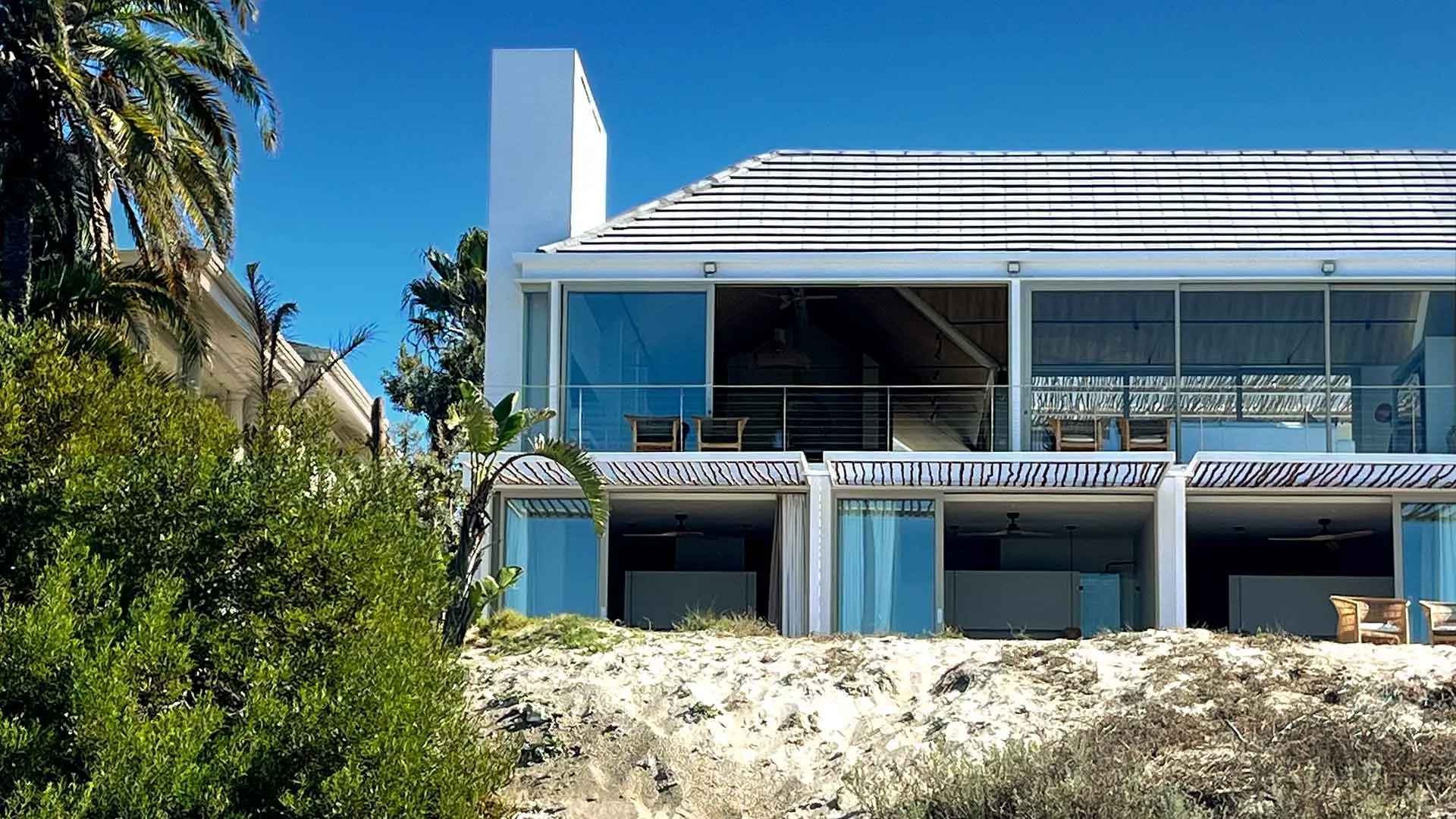 The villa from the beach on a bright day: glass gable above, bedrooms opening under the pergola below