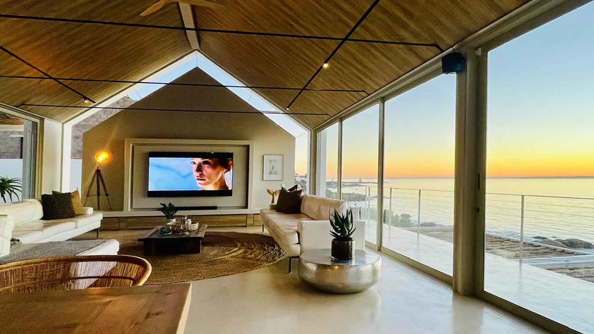 Gabled TV lounge at sunset with the ocean glowing through floor-to-ceiling glass