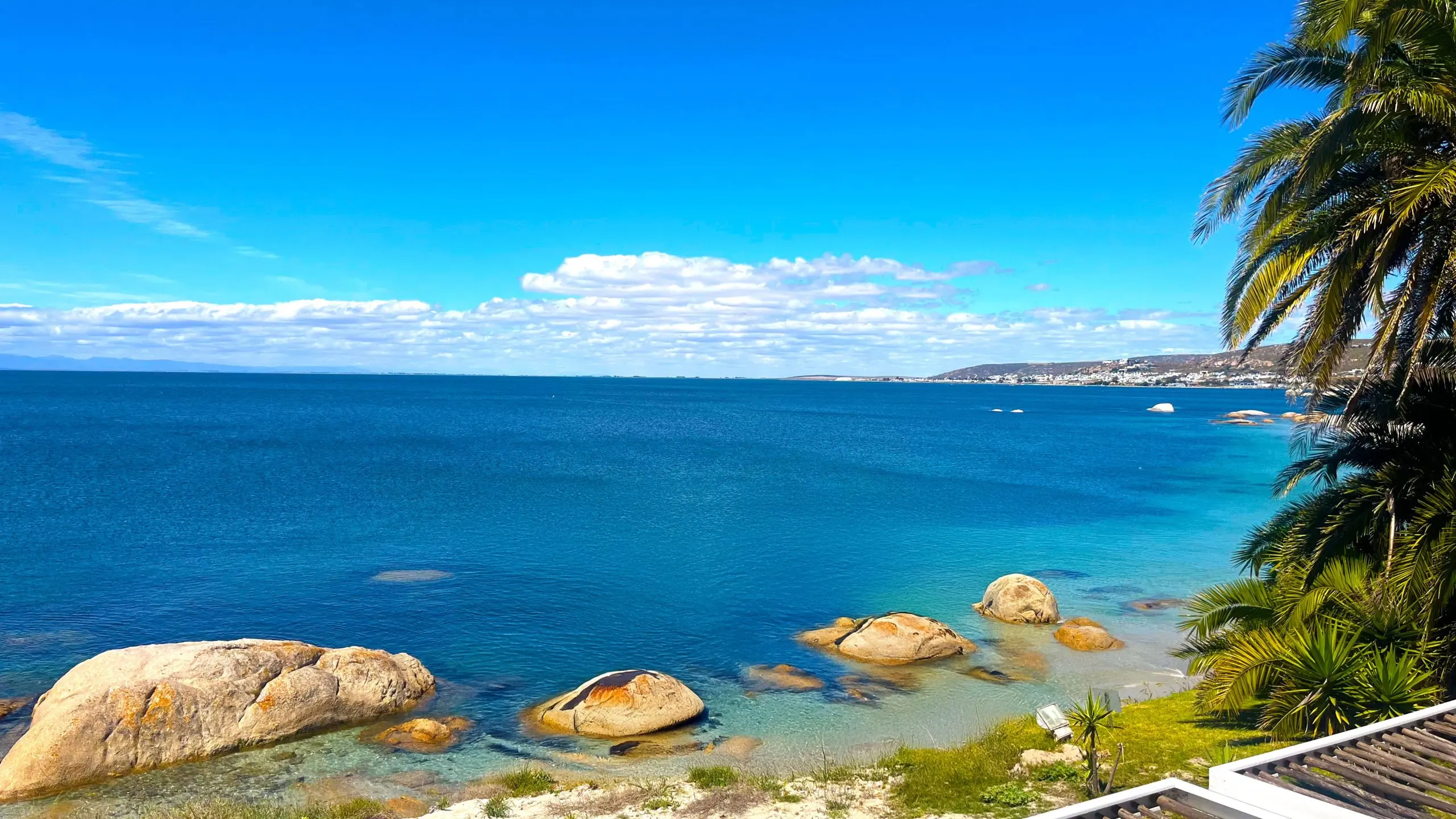The calm turquoise bay in front of the villa, granite boulders in the shallows, palms on the right