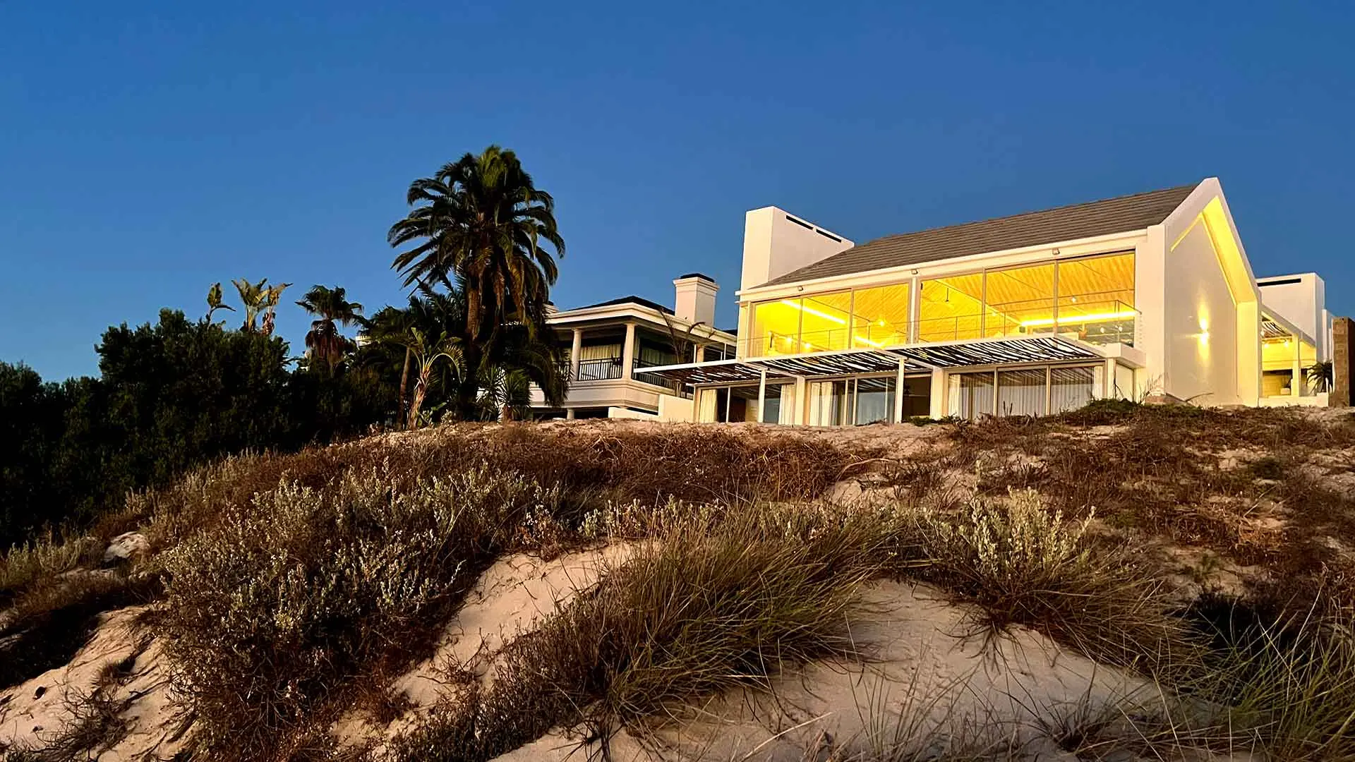 Villa Selah at dusk: the glass gable glowing warm above the dune grass